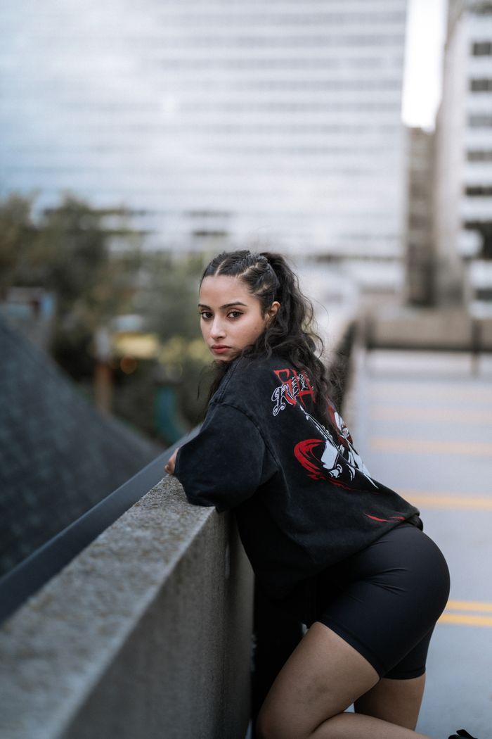 Mastering the First Impression: Your intriguing post title goes here Young woman posing in urban setting, wearing black streetwear. City backdrop offers a modern vibe.